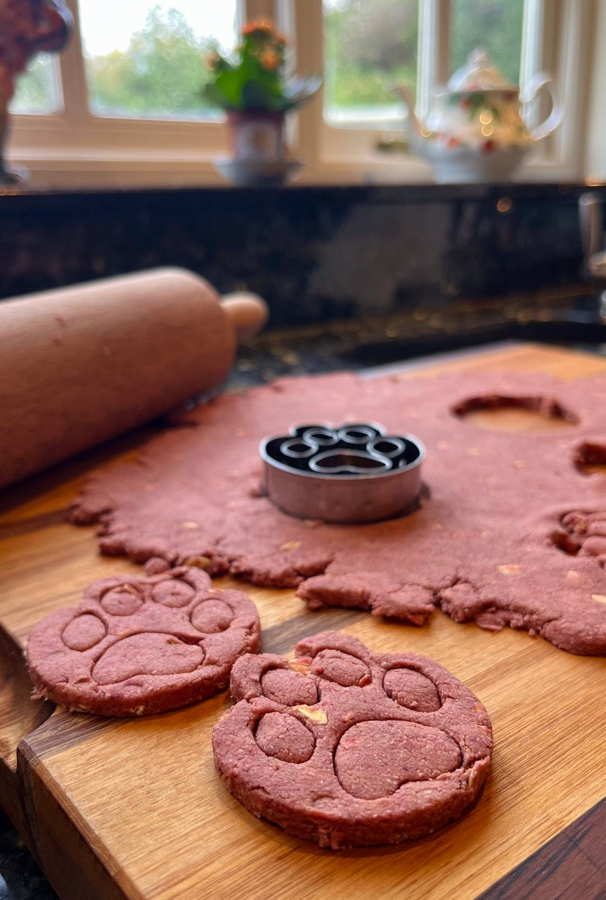 Pawprint cutter cutting shapes from pink beetroot dog treat dough.
