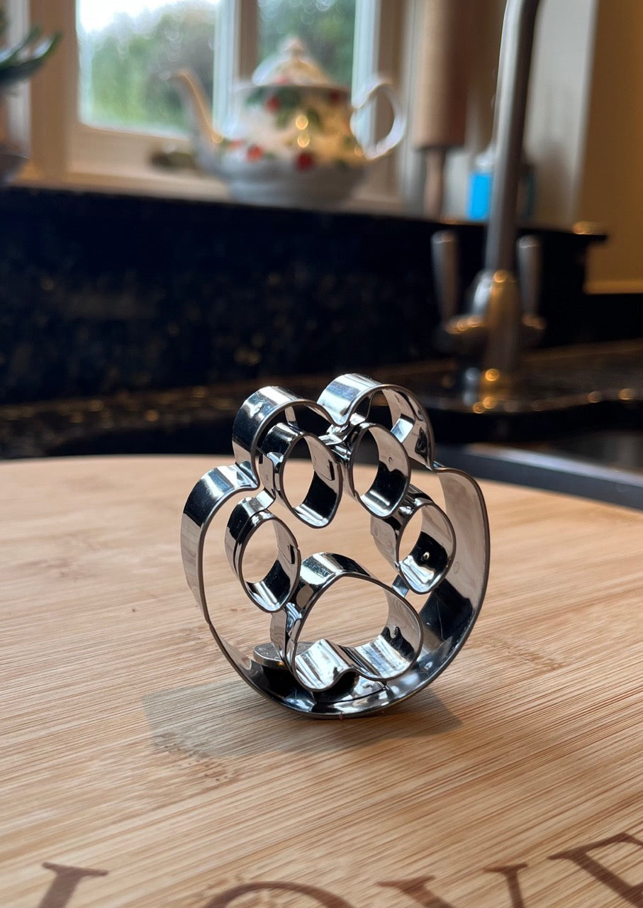 Pawprint cookie cutter standing upright on a wooden cutting board in a kitchen setting.