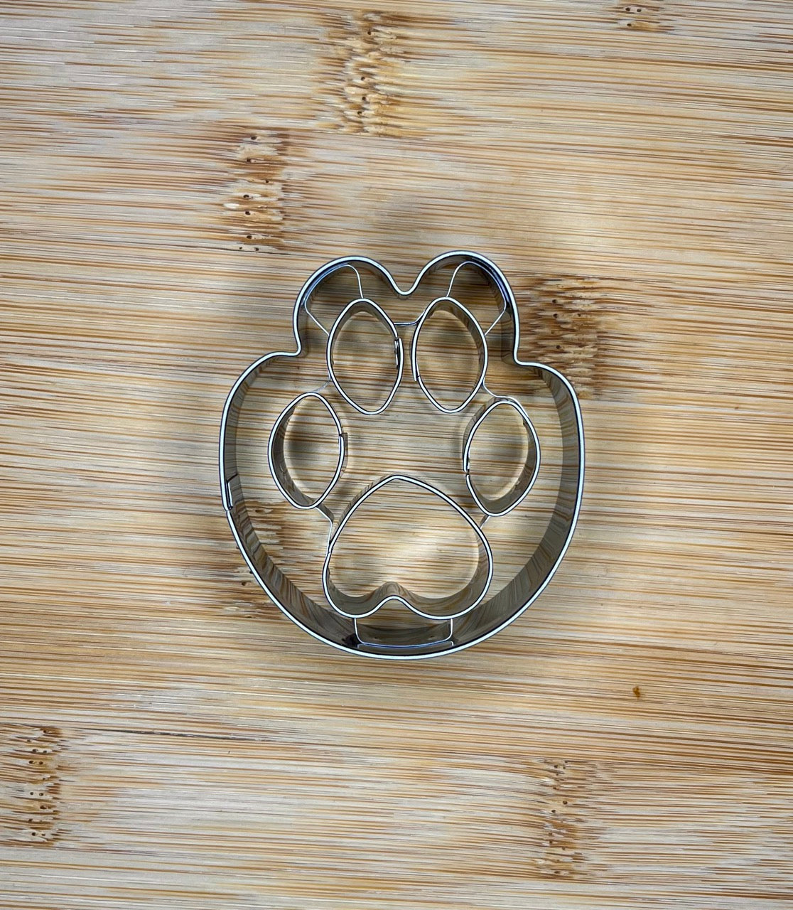 Pawprint cookie cutter laid flat on a wooden cutting board, showing raised toe detail.
