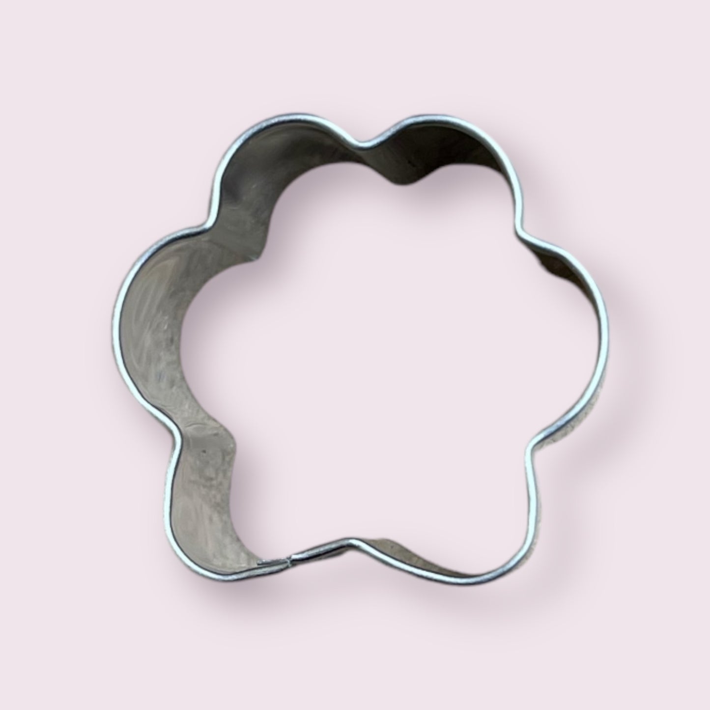 Metal paw-print cookie cutter on pastel background from BarkyBakey.